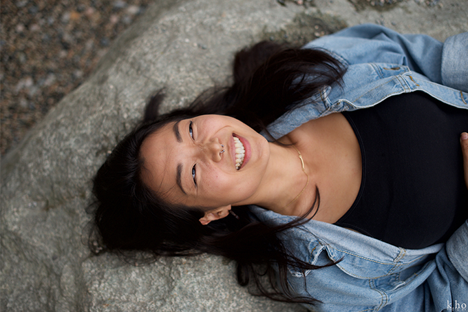 Romi Kim lies on a rock and wears a big smile on their face