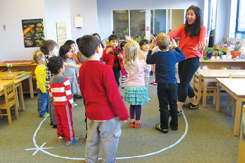 A group of kids stand in a circle around an adult with an excited expression on their face